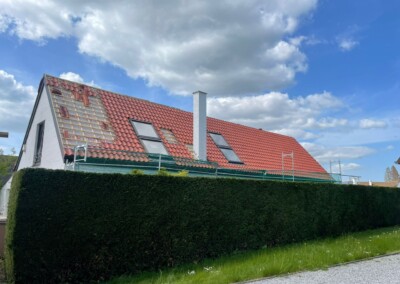 Maison avec couverture toiture en tuiles rouges, fenêtres de toit, et une grande haie verte